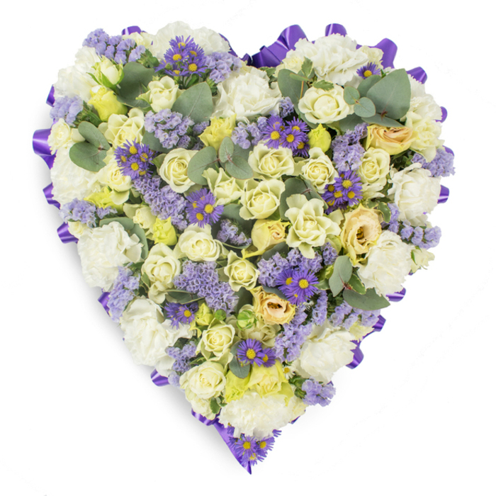 This meticulously arranged heart-shaped floral tribute is presented on a stark white background so each detail reads clearly: a neat, continuous purple satin ribbon outlines the entire heart, its gentle folds catching soft studio light and lending a formal, finished edge. The interior is a harmonious weave of soft whites, creams and pale yellows-countless cream and pale yellow roses form the principal texture, their petals layered from tight buds to softly opening faces and occasionally showing a pale green undertone that adds subtle depth. Lush white carnations are placed to build volume and a reassuring, classic presence. Scattered through the massing are clusters of lavender-hued statice, their tiny blossoms creating a light, whispery texture, and vivid small purple aster-like flowers with bright yellow centers that bring concentrated accents of colour and visual rhythm. Rounded eucalyptus leaves in a dusty blue-green break the floral plane with organic shape and a cool scent-suggestion, helping the heart feel grounded and contemporary. The overall effect is one of calm dignity: a peaceful, comforting composition suited to funeral services, wakes or graveside memorials in Forest Gate or nearby chapels along Forest Lane and Stratford High Street. The arrangement reads as both an artisan floral statement and a tender emblem of enduring love and remembrance, crafted to offer solace through restrained beauty and considered floral technique.