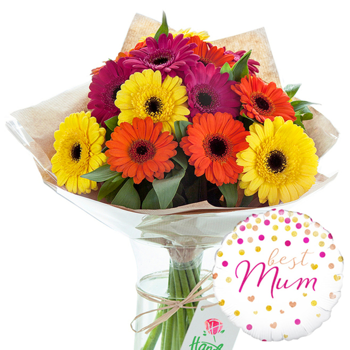 In this carefully composed studio image, a hand-tied bouquet of gerbera daisies takes centre stage, glowing with colour against a simple white backdrop that could easily be the front counter of a Forest Gate flower shop. The arrangement is generous and rounded, made up of around a dozen large gerbera blooms, each one fully open and evenly spaced so the viewer can appreciate every detail. Bold shades of sunny yellow, zesty orange, and deep magenta-fuchsia blend together, their flat, radiating petals creating a joyful ring around the darker, textured centres characteristic of gerberas. Dark green leaves and a little foliage are tucked between the heads, adding natural shadows and depth while suggesting freshness, as if these stems had just arrived from a local market not far from Woodgrange Road. The bouquet is wrapped first in a sheet of rustic, light brown kraft paper, its soft creases and matte finish adding an earthy, handmade charm. This is encased in a clear, glossy cellophane layer that gently crinkles and catches the light, giving a polished, ready-to-gift appearance suitable for doorstep delivery anywhere around Forest Gate. At the base, natural twine or raffia is tied in a modest bow, emphasising the care and human touch involved in the tying. The stems are placed upright in a tall, slim glass vase filled with clear water, so the clean green lines of the stems remain visible and ordered. To the lower right, a round white balloon completes the gift. Its surface is dotted with scattered pink, orange, and metallic gold confetti spots and tiny hearts, and the affectionate message best Mum appears in fluid pink script at the centre. Together, the flowers and balloon create a warm, celebratory gift that feels perfect for Mother's Day, a birthday, or any occasion when someone in Forest Gate wishes to express appreciation, love, and joy in a vivid, tangible way.