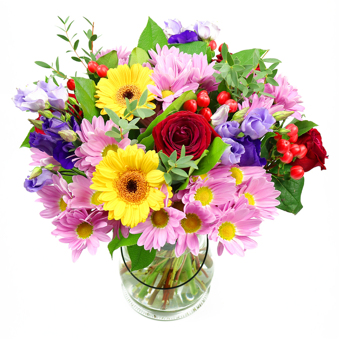 In this image, a lush, mixed bouquet bursts from a clear glass vase, its colours intensified by the clean white studio background. Deep red roses form the emotional core of the design, their tightly layered, velvety petals spiralling inward and drawing you close, like a whispered message of affection sent across Forest Gate to someone dear. Just above and alongside them, bold yellow gerbera daisies with dark, toasted centres lift their broad faces outward, bringing an immediate sense of happiness and open-hearted warmth, the way sunshine spills along the high street on a bright morning. Encircling these focal blooms is a soft halo of pink and lavender daisies or chrysanthemums, their many fine petals creating a feathery, almost cushion-like texture, while small golden centres add delicate points of light. Woven through the daisies, strands of purple and lilac lisianthus stretch gracefully, their bell-shaped flowers slightly flared and gently ruffled, adding depth, movement and a cool, sophisticated note that balances the richer reds and yellows. Red hypericum berries, plump and glossy, peek out from between the petals, giving the arrangement playful dots of texture and a contemporary flair that would suit a modern home near Manor Park or a stylish gathering in a Forest Gate flat. Supporting everything is an abundance of greenery in multiple tones, from dark, broad leaves that provide structure to lighter, more slender stems that arc outwards, giving the bouquet a natural, garden-inspired silhouette. Through the transparent vase you can see the neatly spiralled stems and clear water, small details that reflect the precision and pride of a skilled local florist. The overall impression is of a generous, celebratory arrangement-ideal for birthdays, congratulations, or simply to bring comfort and colour to a quiet corner-radiating the friendly, community spirit of Forest Gate.
