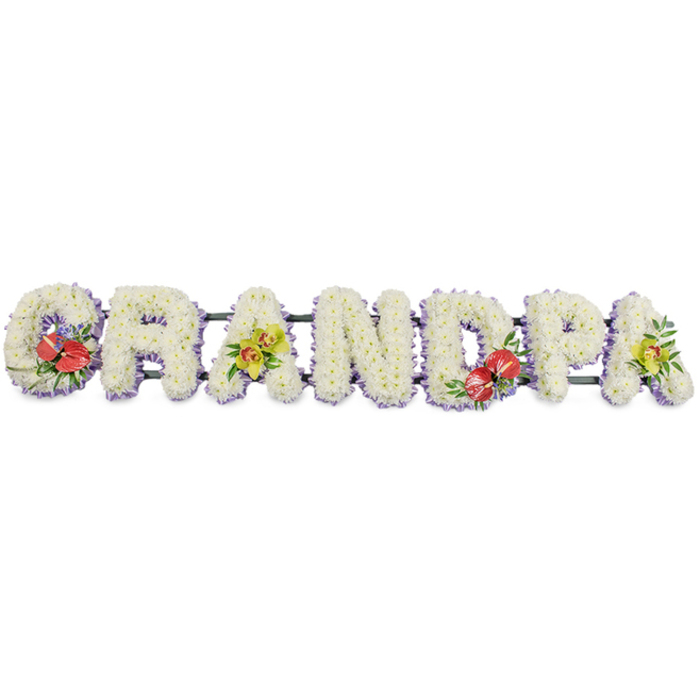 This image shows a striking, full-length floral tribute that clearly spells "GRANDPA" in upright, three-dimensional letters, presented against a bright white studio-style background so the flowers appear crisp and luminous. Each character is shaped by a dense covering of white chrysanthemums, their small, uniform blooms packed closely together to create a plush, cushion-like surface. The texture is soft but substantial, suggesting both gentleness and solidity, much like the presence of a cherished grandfather. Around the base of each letter, a trim of light purple or lavender ribbon adds a discreet band of colour, giving definition and a touch of elegance without detracting from the serene whiteness. Running behind the word is a dark green framework that supports the letters, mostly hidden yet lending structure-much as the quiet support of family runs beneath a funeral service in Forest Gate or nearby Upton Park. Four accent sprays introduce deeper tones and focal points. The "G" and "D" are adorned with vivid red anthurium flowers, their waxy, heart-shaped bracts and protruding spadices gleaming against glossy foliage and small purple filler flowers, adding a sense of passion, memory, and gratitude. The first and last "A" feature soft clusters of yellow-green cymbidium orchids, their sculpted blooms and fresh lime colour providing a sophisticated contrast that hints at renewal. Crafted with care by a professional local florist, this bespoke funeral arrangement would sit beautifully beside a coffin or at the front of a service, offering the family in Forest Gate a personalised way to honour "Grandpa" with flowers that feel both traditional and thoughtfully designed.
