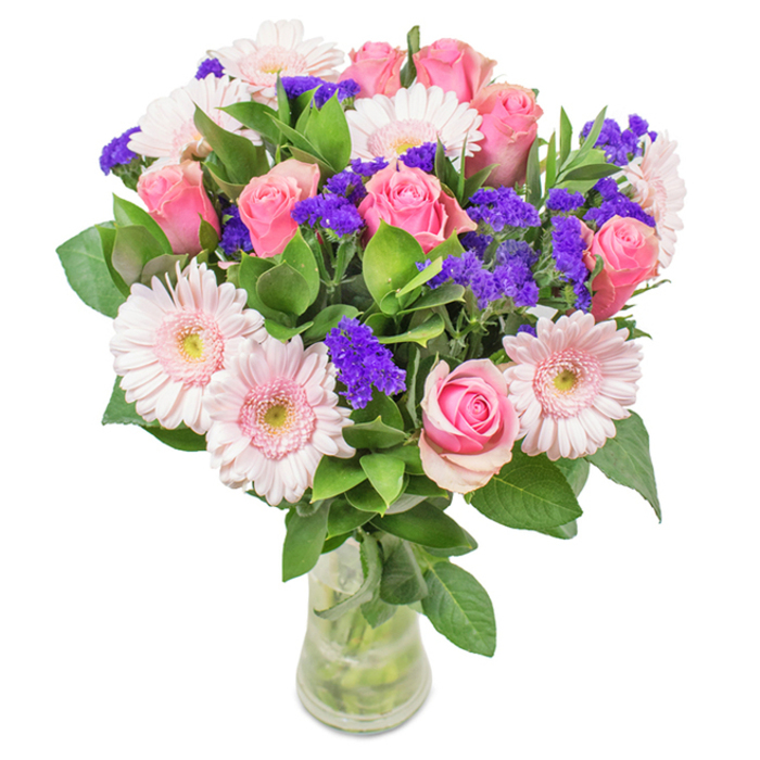 A stunning, thoughtfully arranged bouquet set against a pristine backdrop, expertly presented in a tall clear glass vase near Forest Gate. At its heart, around eight to nine medium pink roses-some tenderly furled, others just beginning to spiral open-recall moments of affection by Wanstead Flats. Flanked by pale pink gerbera daisies with broad, luminous faces and faintly blushed centers, the arrangement is artfully balanced and brimming with gentle colour. Clusters of vibrant purple statice, reminiscent of blossoms gathered from local gardens on Capel Road, weave through the foliage, adding rich visual punctuation and a pleasing contrast of texture. Lush, kaleidoscopic greenery grounds these blooms, suggesting abundance and freshness with every glance. Through the vase's clear lines, stems and ripples of water remind the viewer of a fresh delivery arriving at a front door off Woodgrange Road. This Forest Gate bouquet, carefully crafted for special occasions or everyday delight, conveys a sense of cheerful elegance, celebration, and heartfelt sentiment-suited for birthdays, anniversaries, or simply honouring the joys of community living.