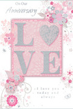 In this close-up, an anniversary card is styled with the same refined romance you might expect from a carefully chosen Forest Gate bouquet. The design centres on the word LOVE, each capital letter raised slightly from the card and edged with a delicate dusting of silver-toned glitter. The effect is both visually striking and gently tactile, encouraging fingertips to pause and trace the shapes. Behind the word lies a blush pink panel with a soft, luminous finish, surrounded by a backdrop of pearly white and hints of pale silver that lend the whole card an almost dreamlike glow. Around the central motif, intricate illustrations of flowers, leaves, and fine curling stems drift across the surface, echoing the lines of a florist's pencil as they sketch a romantic arrangement for delivery off Woodgrange Road. The blossoms are rendered in muted shades of pink and grey, with occasional touches of silver that catch the light like dew on petals, while the spacing of the illustrations keeps the card feeling airy and uncluttered. Along the top or bottom, in a graceful, flowing script, are simple, heartfelt anniversary sentiments-phrases of lasting love and gratitude that match the card's gentle mood. The overall palette of blush, white, and silver feels soft and intimate, ideal for marking a milestone shared quietly at home or over dinner in a favourite local spot. It is the paper equivalent of a pastel arrangement delivered in Forest Gate: understated, romantic, and rich with meaning in every carefully considered detail.